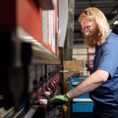 Man with long hair working on red machine in factory.