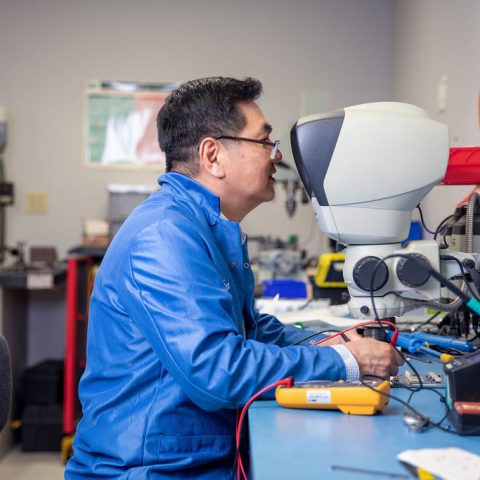 Man working with wires and looking through a microscope