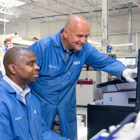 Two men working around a computer screen in a factory