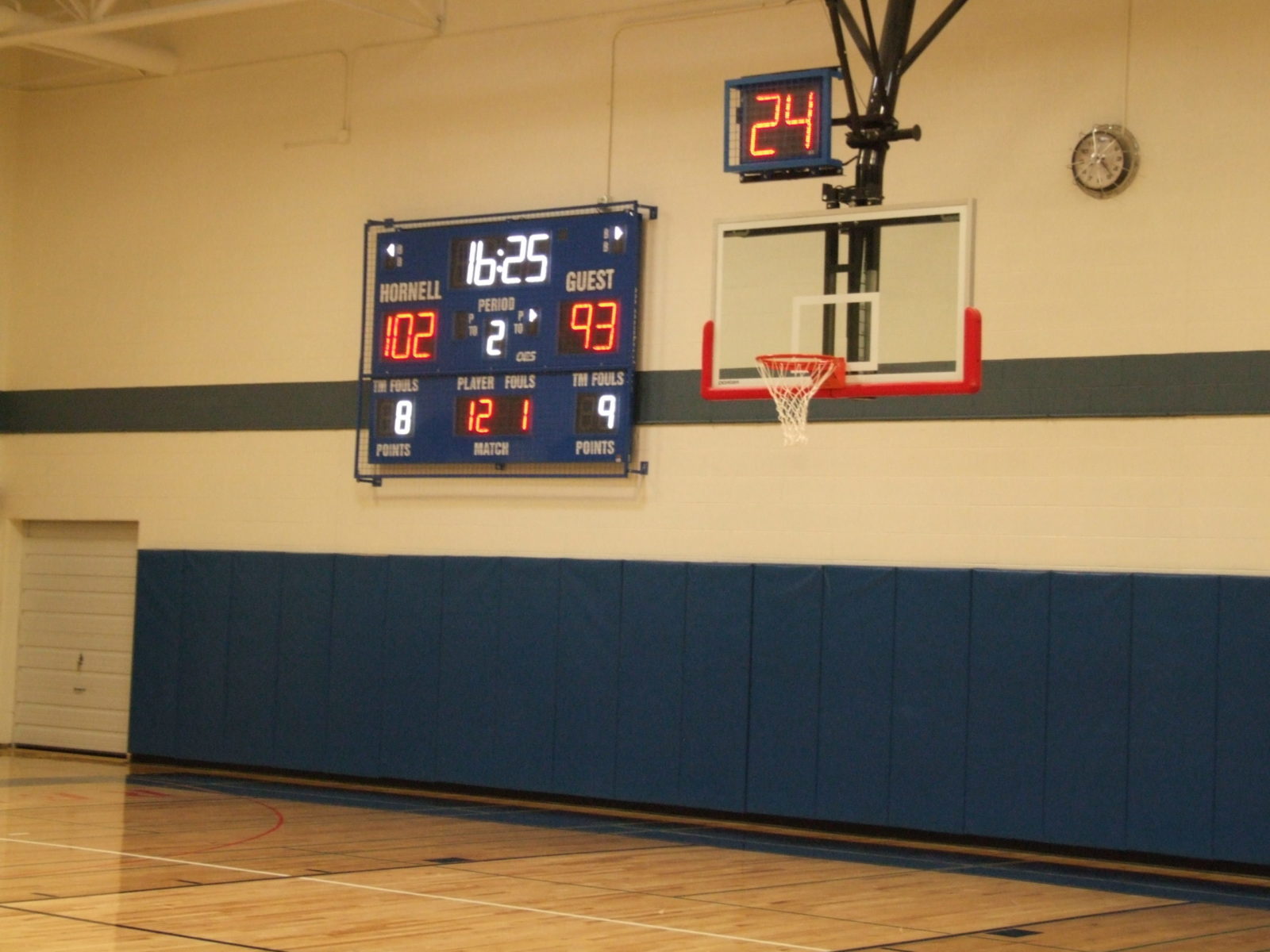 An indoor basketball scoreboard with a shot clock above the basketball net.