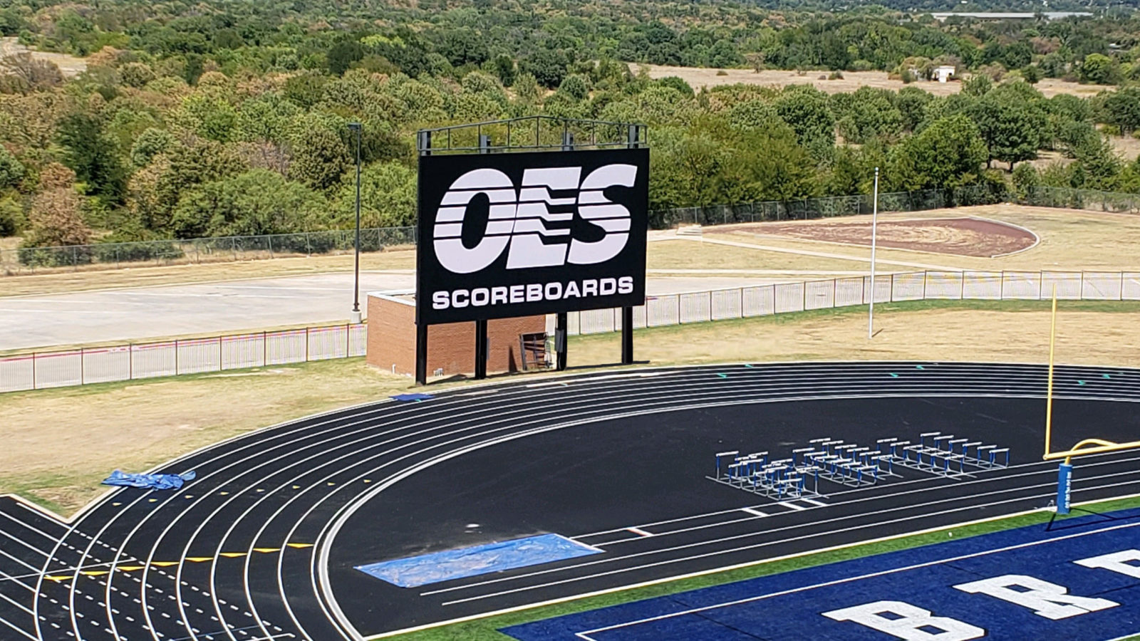 The OES scoreboard logo displayed on a new scoreboard next to an outdoor track.
