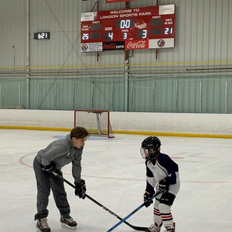 Young hockey player and his coach in front of the net and scoreboard