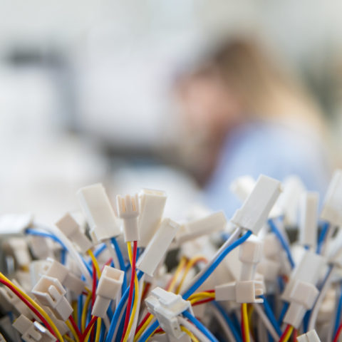 The white ends of brightly coloured wires, with two women blurred out in the background.