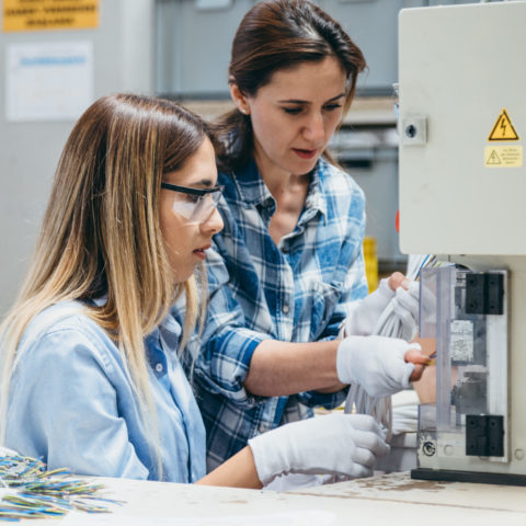 Two women working together putting wires into a smaller machine.