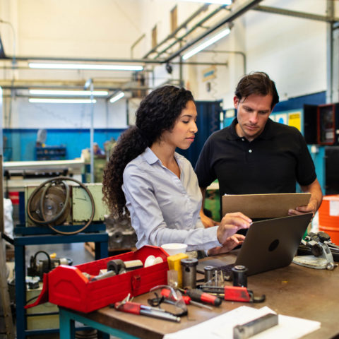 A man and women looking at computer screen on a factory floor.