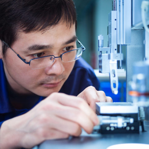 Man working with wires and looking through a microscope