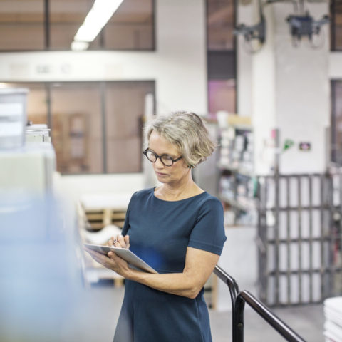 Mature businesswoman on factory floor using digital tablet.