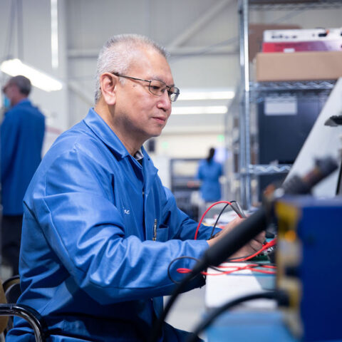 Older man working with wires on factory floor.