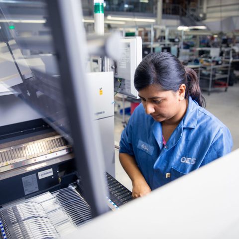 Women in blue lab coat working on factory floor.