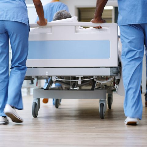 Hospital workers pushing bed down a medical building hallway. 