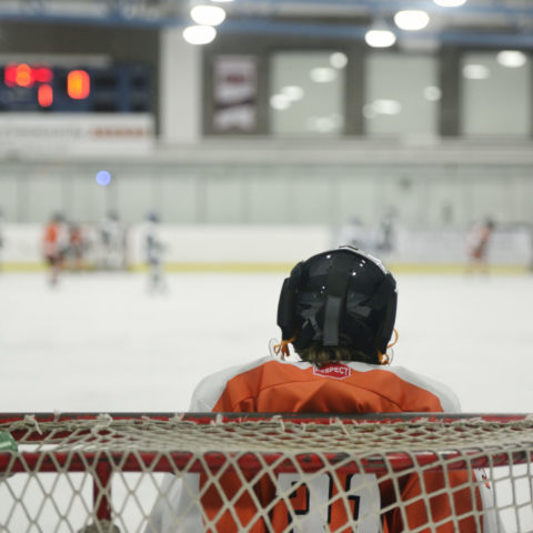 Child hockey goalie in net facing opposition on ice rink