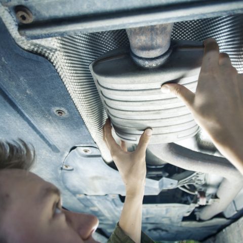 Male mechanic replacing exhaust pipe under car