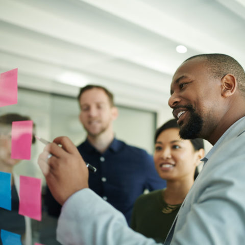 Man pointing at sticky notes while team listens.